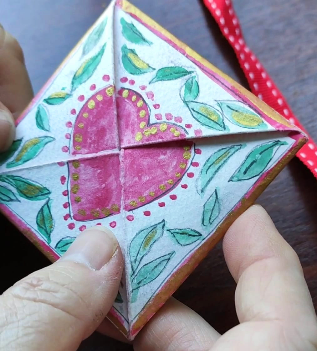 photo of a folded card with a red heart in the centre and a person's fingers holding the paper